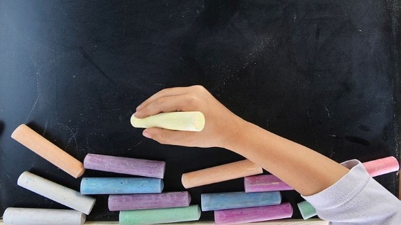 Children's hand holding chalk in front of chalkboard