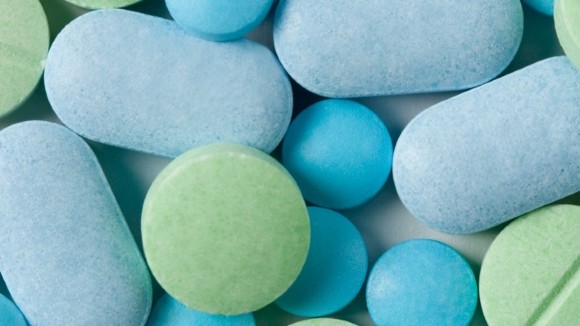 An assortment of blue, green and grey medicine tablets with some tablets layered over others