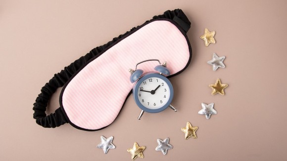 Mask for sleep and alarm clock near it.golden and silver stars around.Circadian rhythms and healthy sleep concept. 