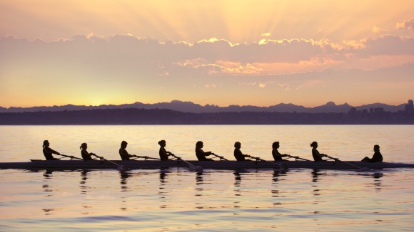 Team rowing boat in bay.