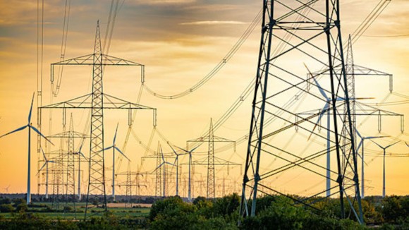 Power grid towers and wind energy turbines in open field.