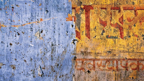 A pock-marked wall in painted in blue and yellow, with Hindi graffiti