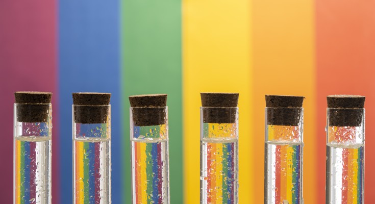 A series of test tubes containing rainbow colours on a rainbow patterned background