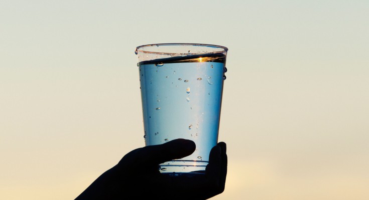 Childs hand holding a cup of water at sunset