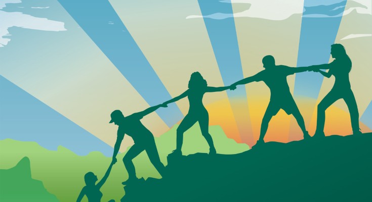 People aligned holding hands to help someone climb a montain