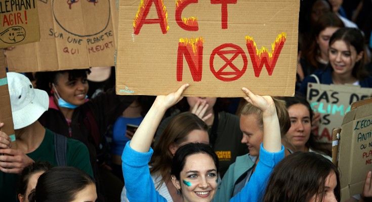 一名妇女在抗议活动中举着一个纸板牌子，上面写着“现在行动”