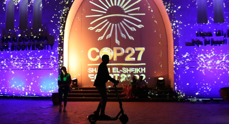 一个骑着电动滑板车的人的剪影在投影的COP27标志前