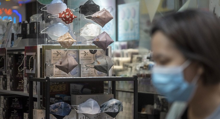 Face masks in shop display with blurred woman, wearing a mask, in the foreground.
