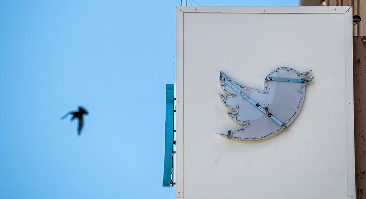 A partially removed sign at Twitter headquarters in San Francisco, California with a distant bird flying across the sky
