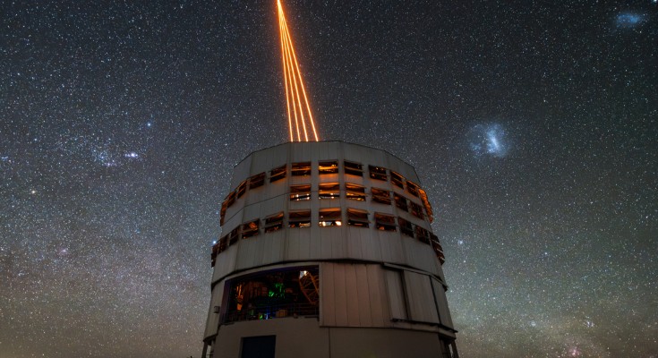 An observatory building emitting four orange laser beams that converge to a point, against a starry sky.