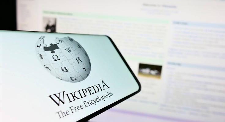 A screen shows the Wikipedia logo, in front of another screen showing the Wikipedia home page