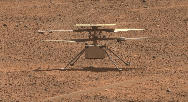 The small helicopter sits on the sandy, red surface of Mars