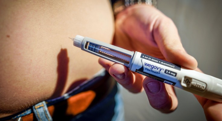 Close up on a hand holding a Wegovy injection pen close to a bare stomach