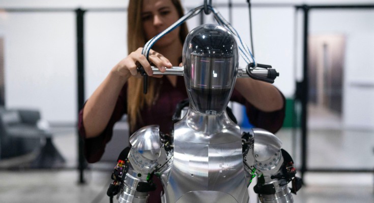 An engineer works on Figure AI's humanoid robot Figure 01 which has a metallic armour-like body and featureless head