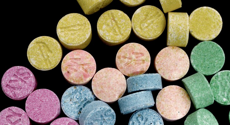 Close-up of MDMA tablets in pink, blue, peach, green and yellow on a black background