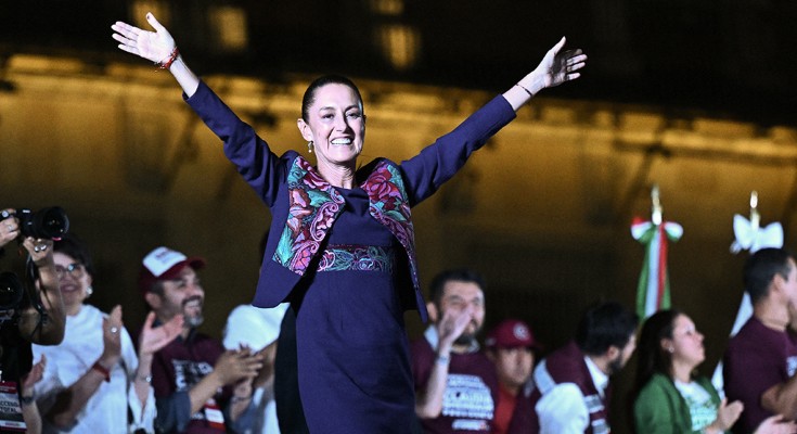 Recently elected Mexican president Claudia Sheinbaum Pardo stands among a crowd with her arms in the air in celebration