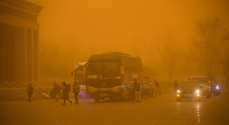 Cars move amid thick sand and dust, turning the sky yellow