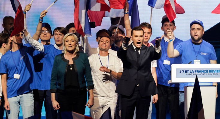Surrounded by flag waving supporters, President of the French far-right National Rally party Jordan Bardella and the party's parliamentary leader Marine Le Pen gesture on stage during an election campaign rally