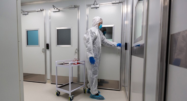 A person in a hazard suit and face mask opens a door in a lab