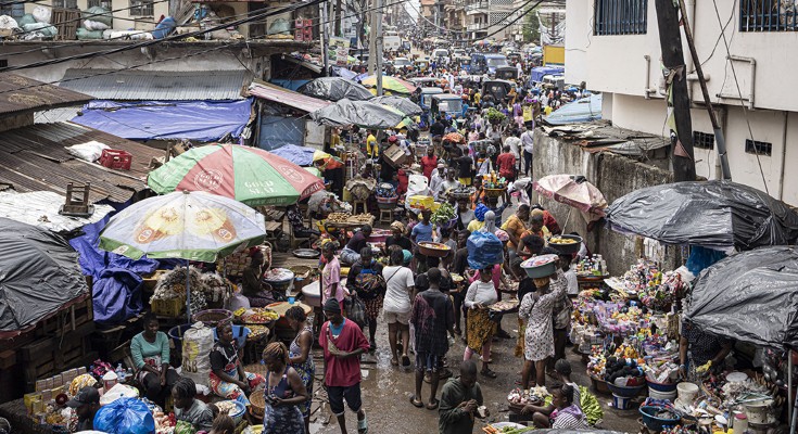 A densely packed street market, with lots of people, water on the ground, and umbrellas over stalls
