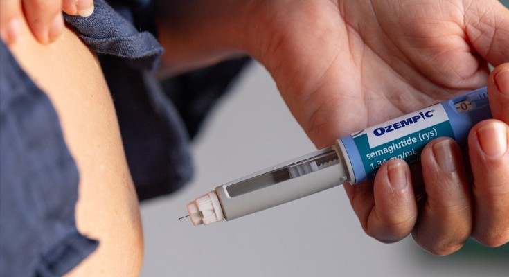 Close up view of a person holding an Ozempic needle injection pen close to their stomach