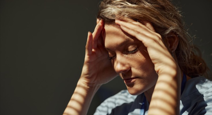 A woman with closed eyes holds her head in her hands