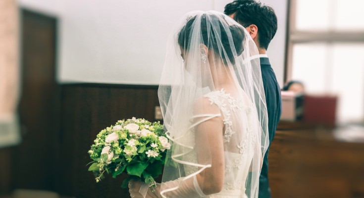 A side view of a woman holding flowers in a white dress and veil arm in arm with a man in a suit