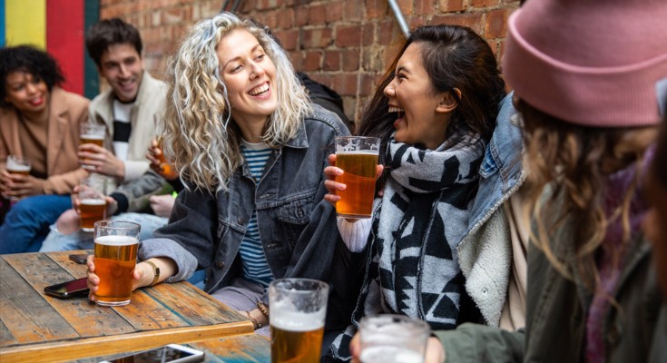 A group of people sat around a pub table, each holding a pint of beer. They're happy and laughing