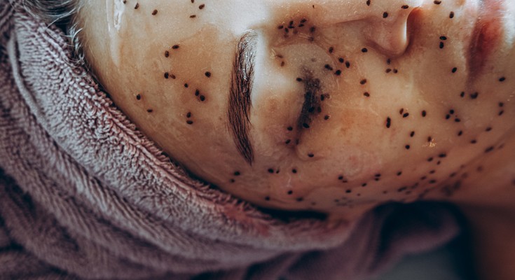 Close-up of woman face with hair towel and an anti-ageing mask with black seeds applied to her face.
