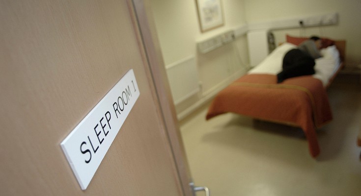 A patient sleeps in a bed, viewed through an open doorway at a sleep clinic