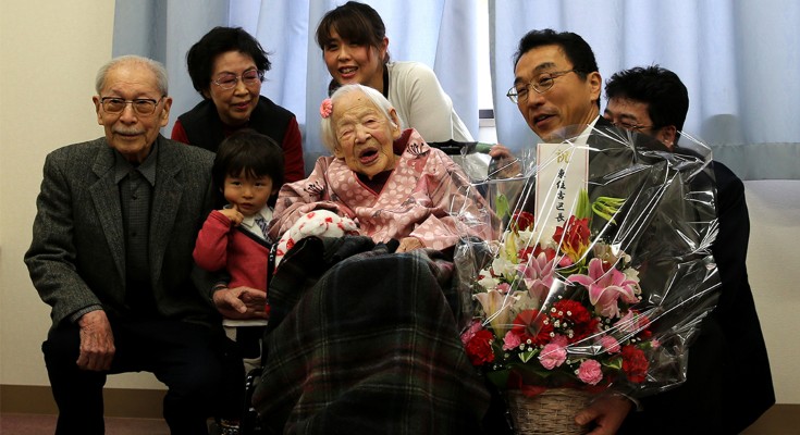 A multi-generational family gathered around the world's oldest woman in a wheelchair, celebrating her birthday.