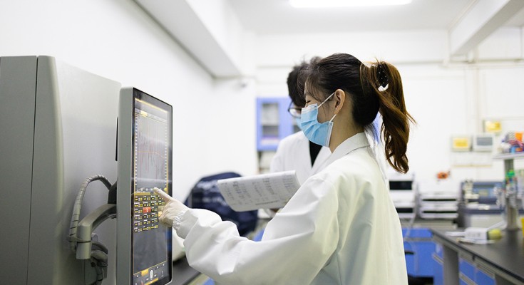 A young female Chinese researcher in a laboratory using a touch screen to programme a machine