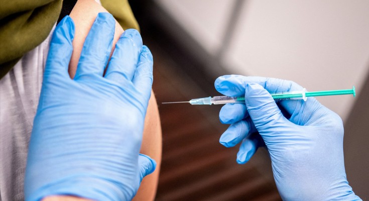 Blue-gloved hands inject a syringe into a person's upper arm