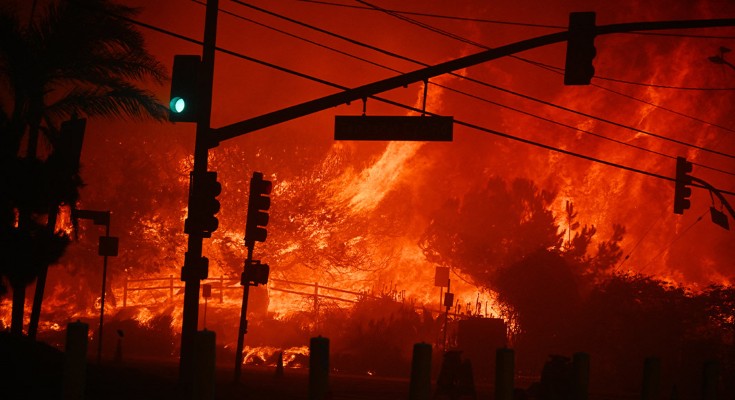 Traffic lights at an intersection are starkly shown in silhouette against the roaring flames of a wildfire