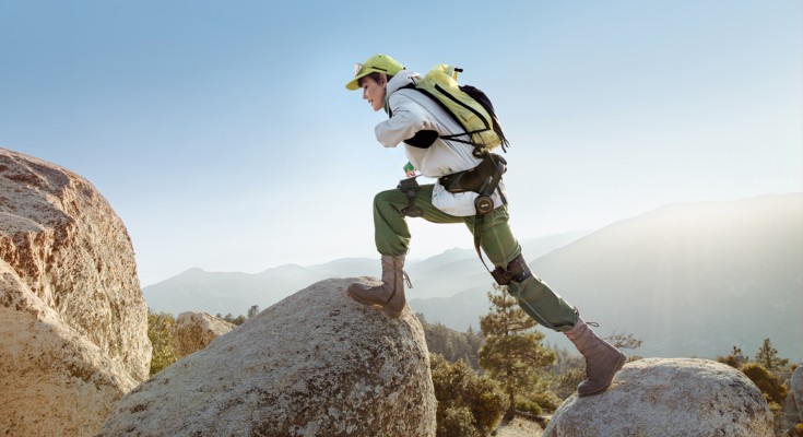 A person using a Hypershell X Series exoskeleton to step up and across from one large boulder to another.