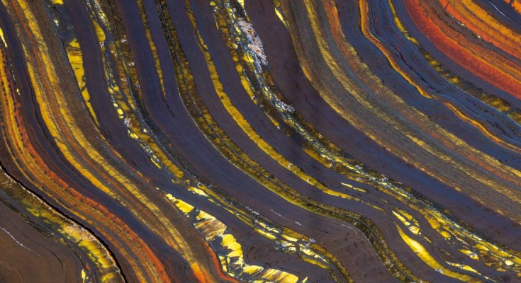 Metamorphosed banded iron formation with dark bands of iron oxides interlayered with gold bands of quartz and amphibole and red-orange bands of chert containing iron oxide inclusions. 