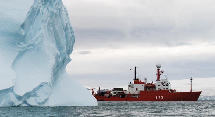 A red ship emerges from behind a large iceberg.