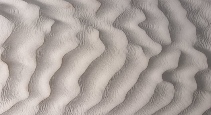 Curving ripples in fine beige sand viewed from above.
